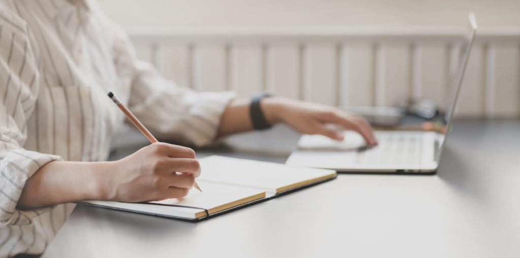 student taking notes in front of laptop