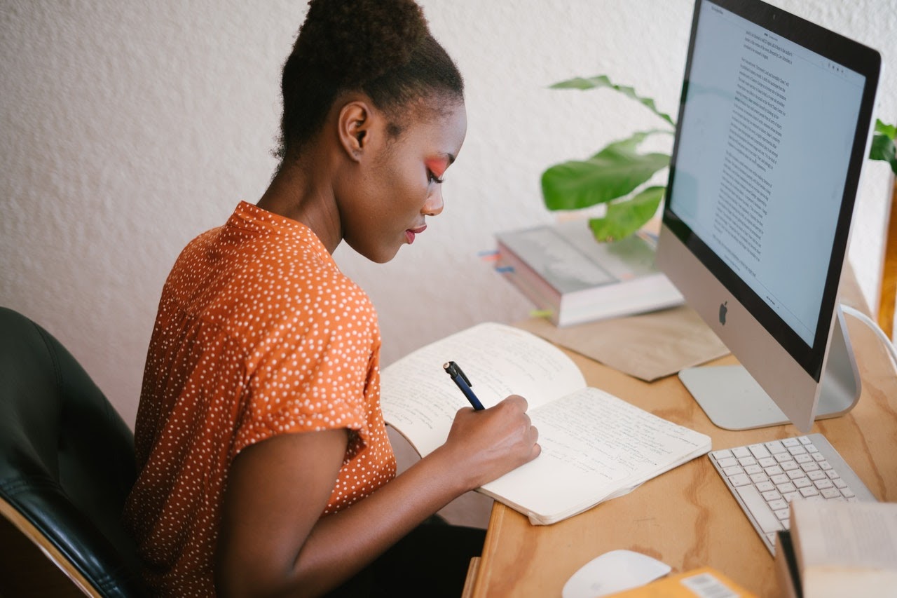 Student writing at desk in front of computer