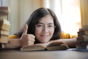 Female student with thumb up leaning on book