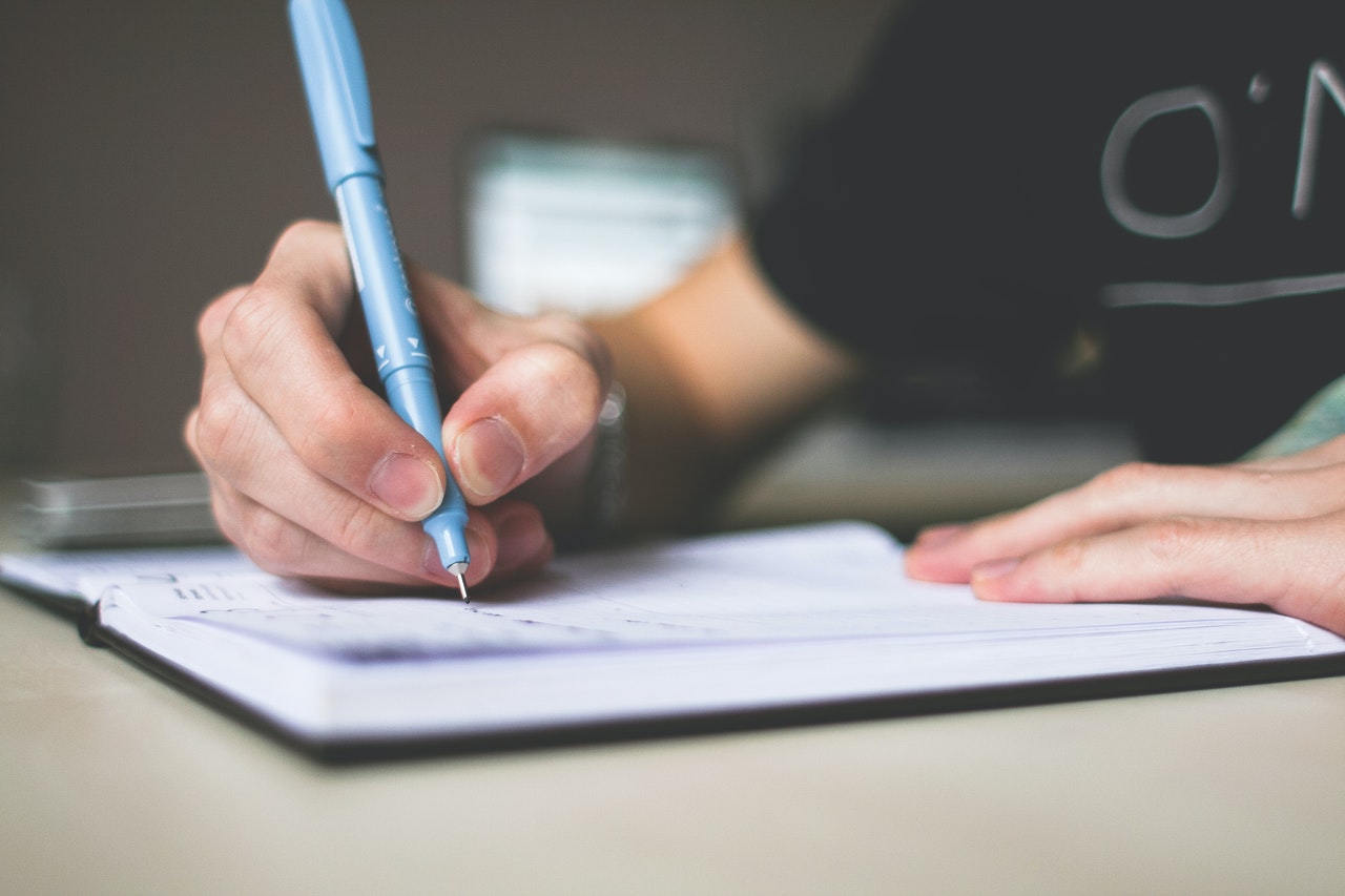 Boy writing with pen on notepad