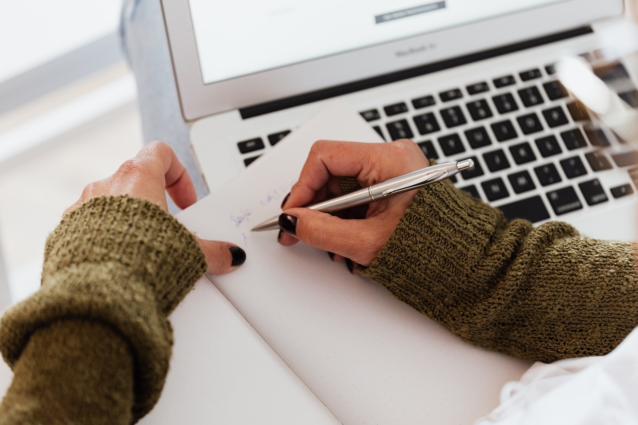 girl writing notes on paper looking at computer