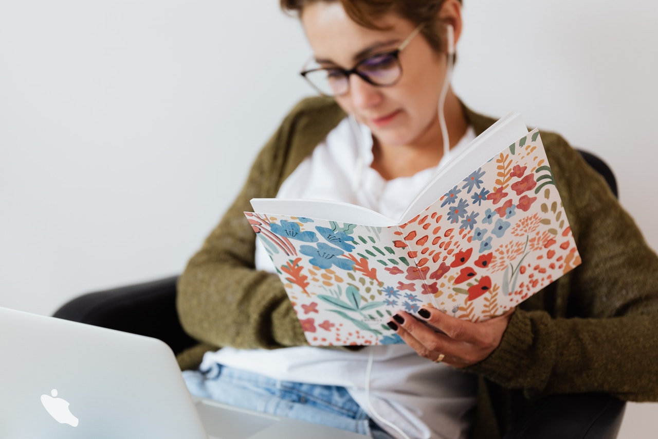 Woman wearing headphones and reading notes from book