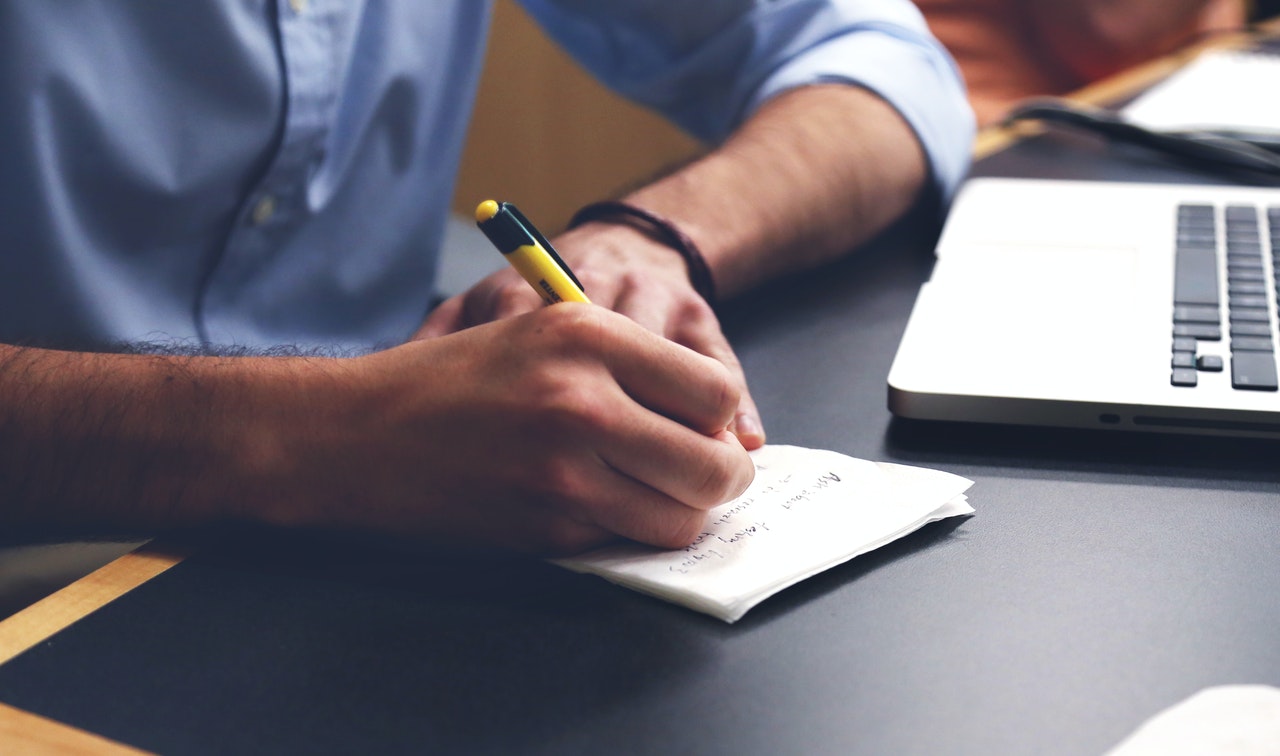 man writing on note pad on desk